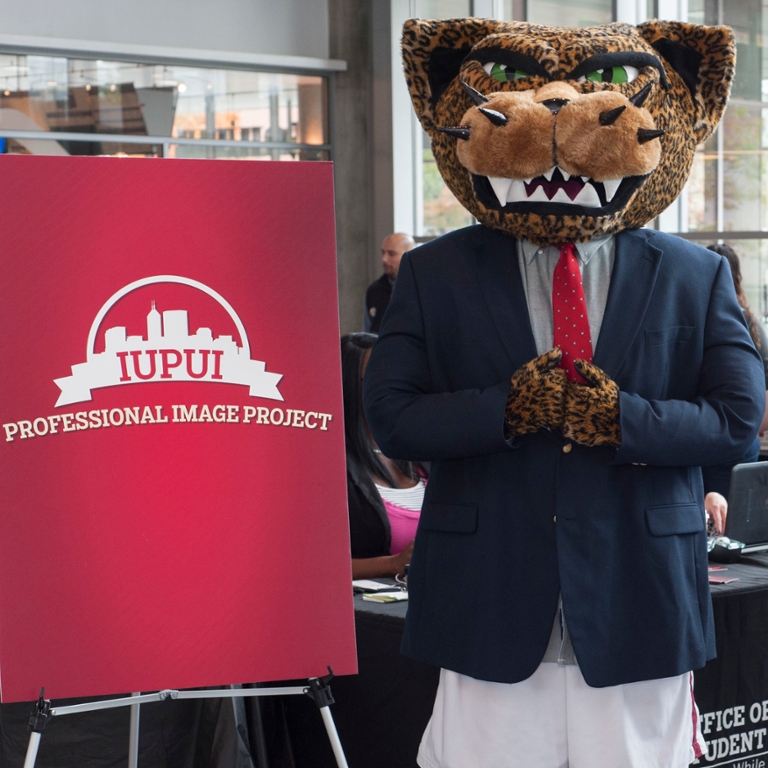 Jawz the Mascot is wearing a suit and standing next to a sign that says IUPUI Professional Image Project.